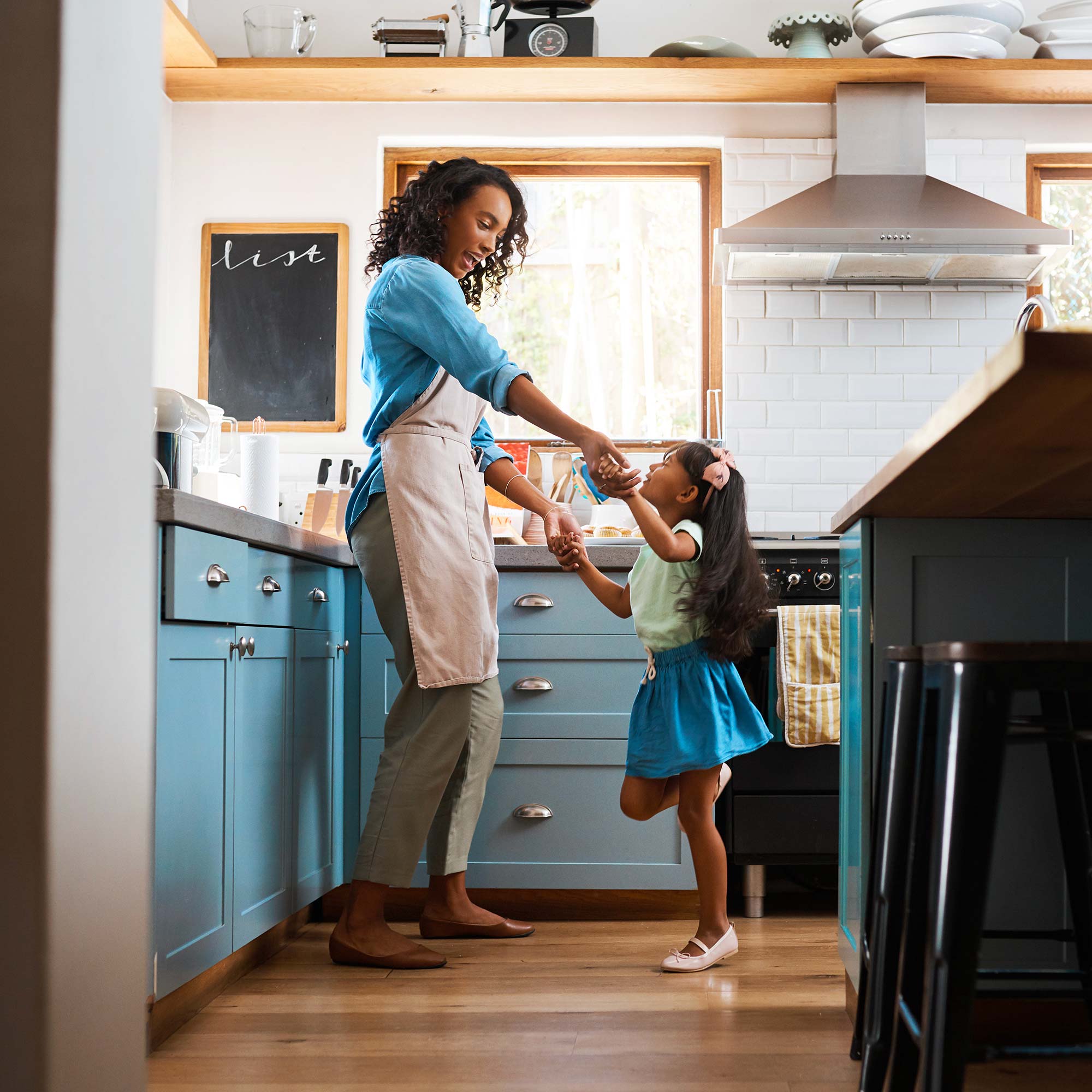 A daughter dances with her mom in the kitchen.